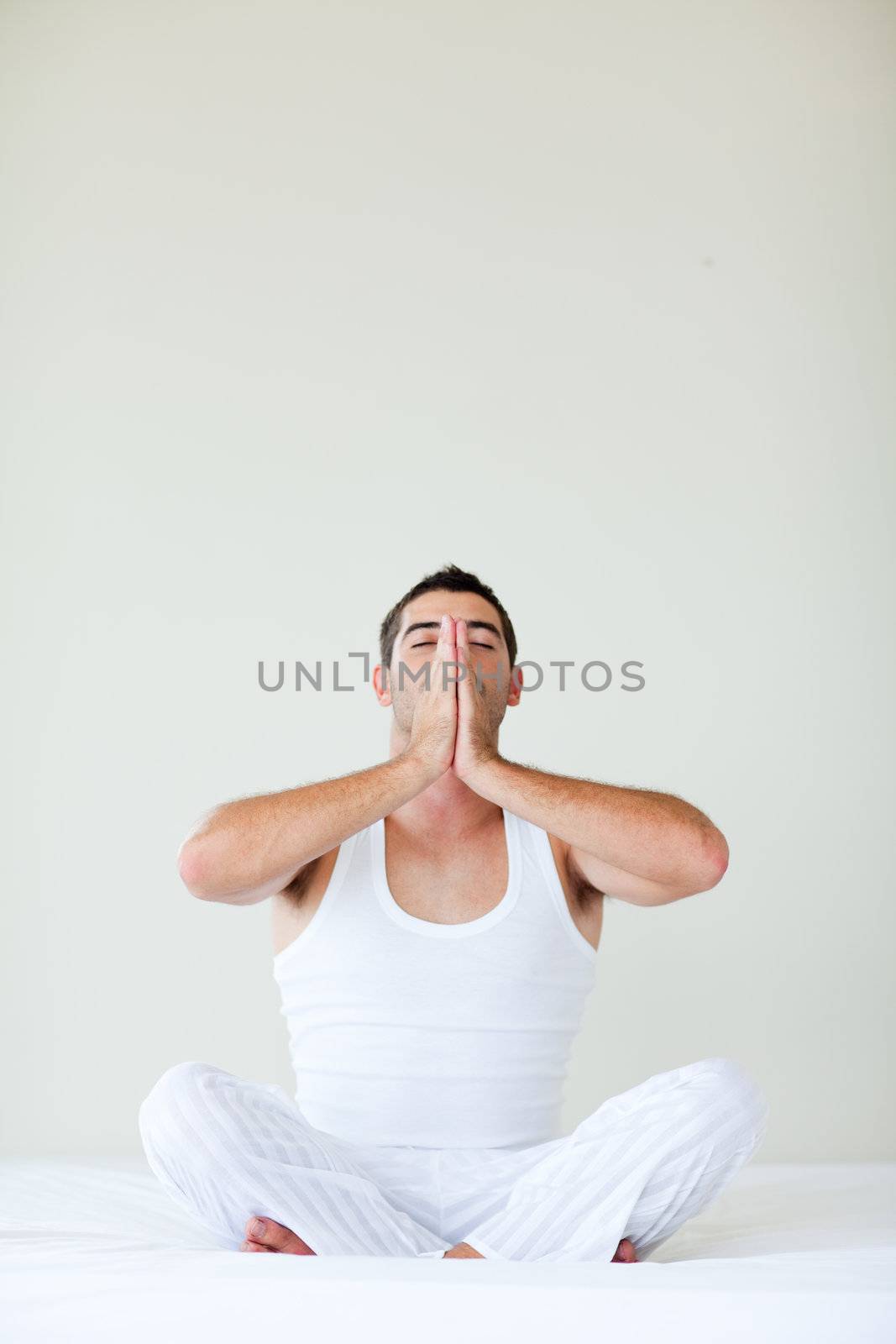 Attractive young man doing yoga sitting in bed