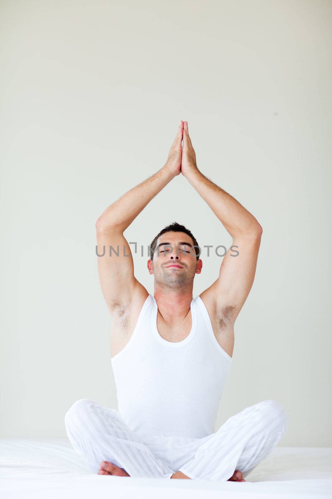 Man sitting on bed doing yoga by Wavebreakmedia