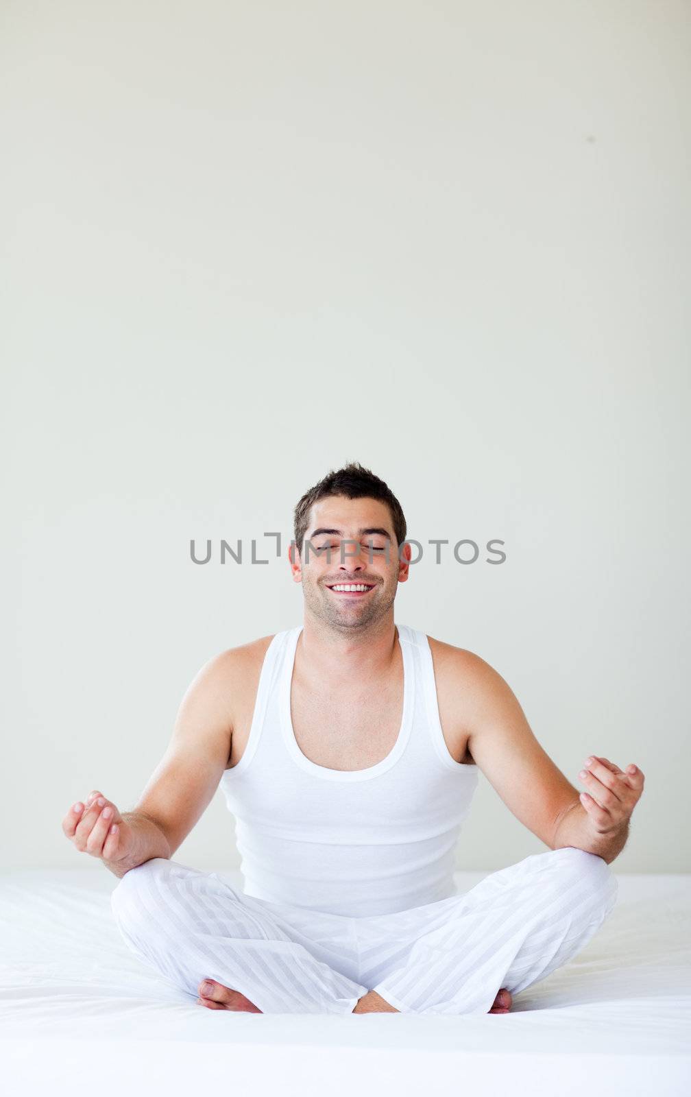Attractive young man doing yoga in bed with copy-space