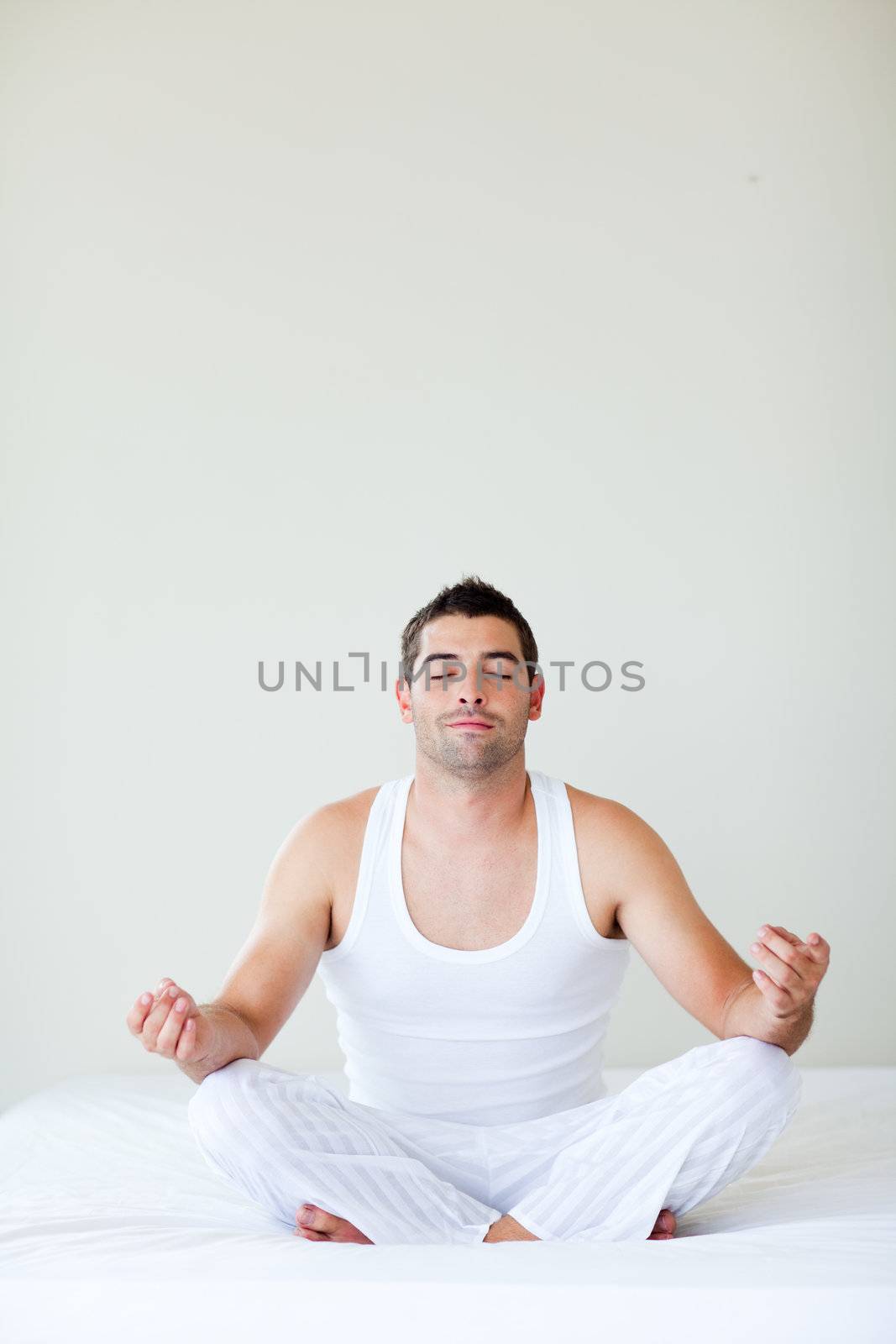 Man sitting on bed meditating by Wavebreakmedia