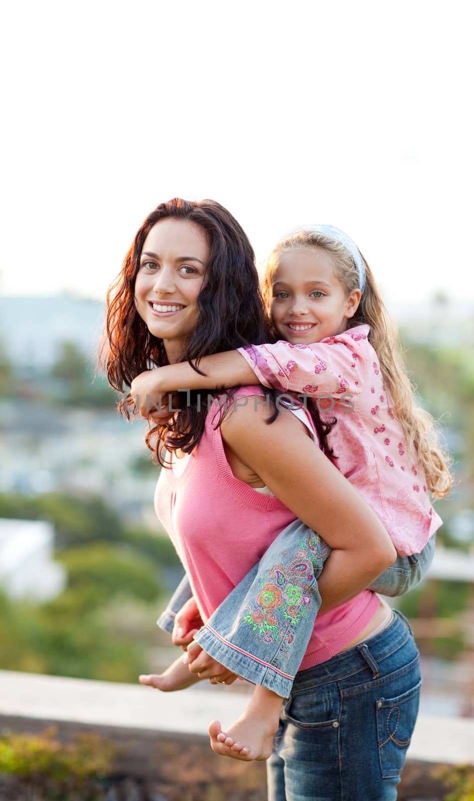 Mother giving daughter piggyback ride outdoors by Wavebreakmedia