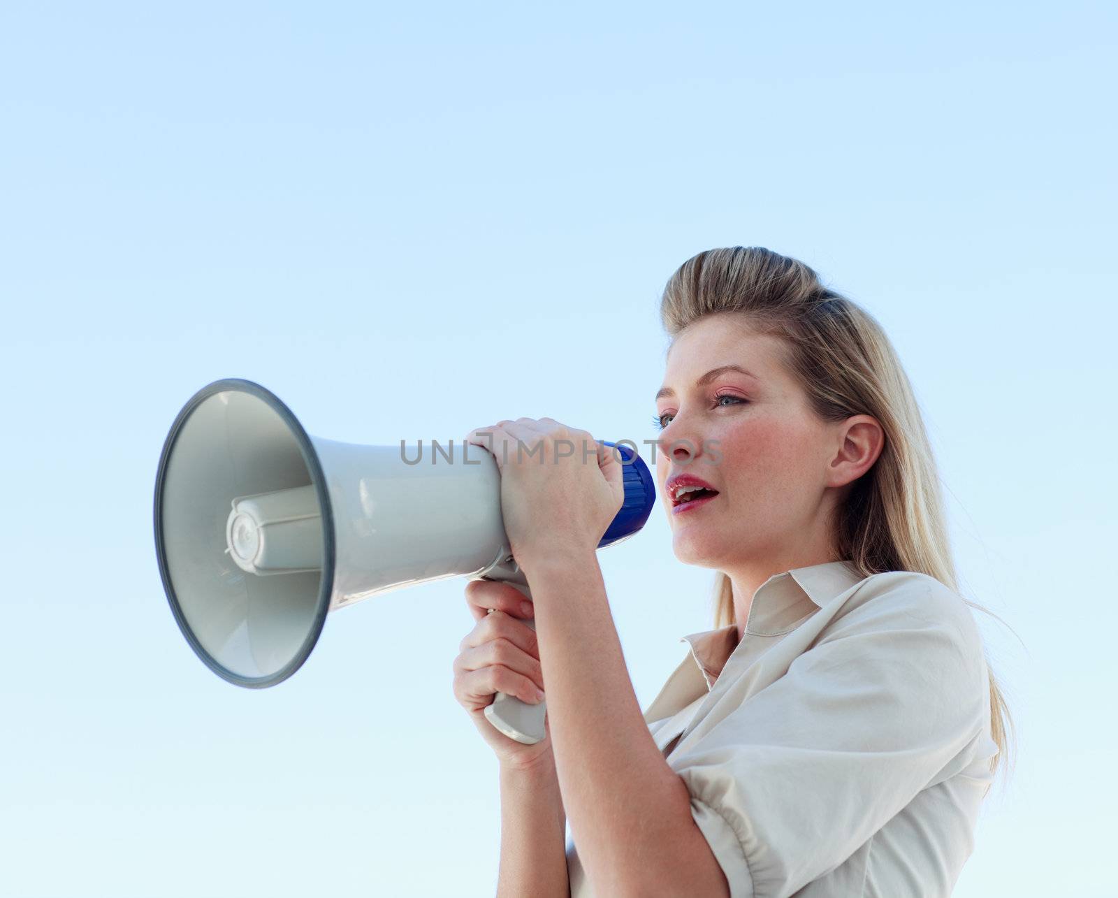 Blonde businesswoman shouting through megaphone outdoors
