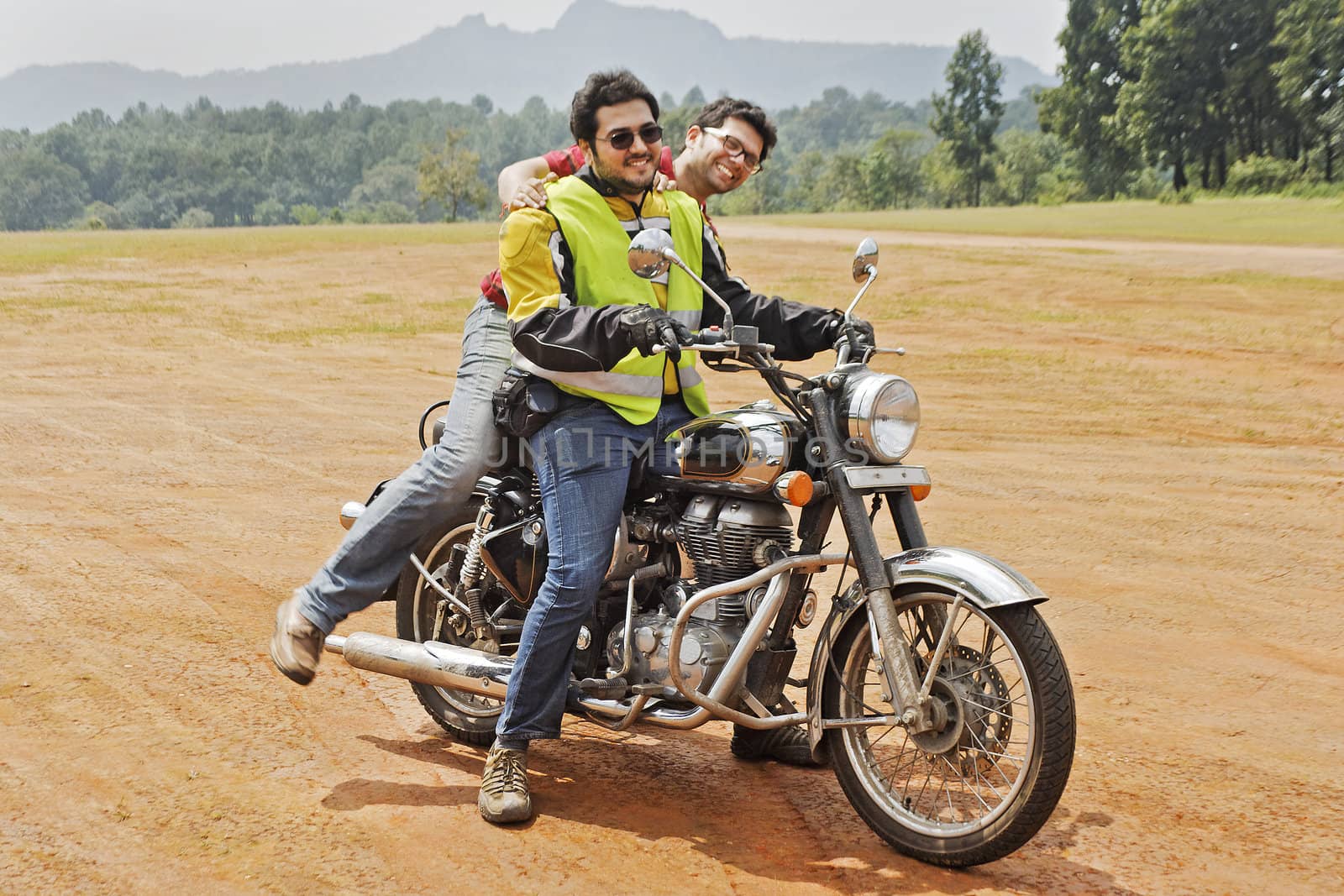 Pillion gets leg over to mount motorbike with rider on off road circuit in rural countryside. Location of shot, Pacharhi, Madhya Pradesh India