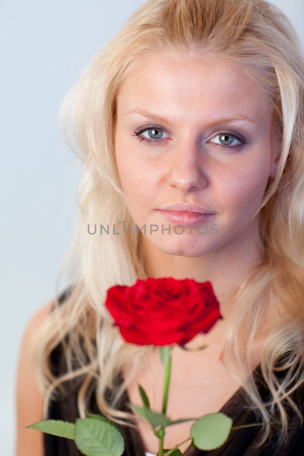 Beautiful blonde woman with a red rose looking at the camera with focus on woman