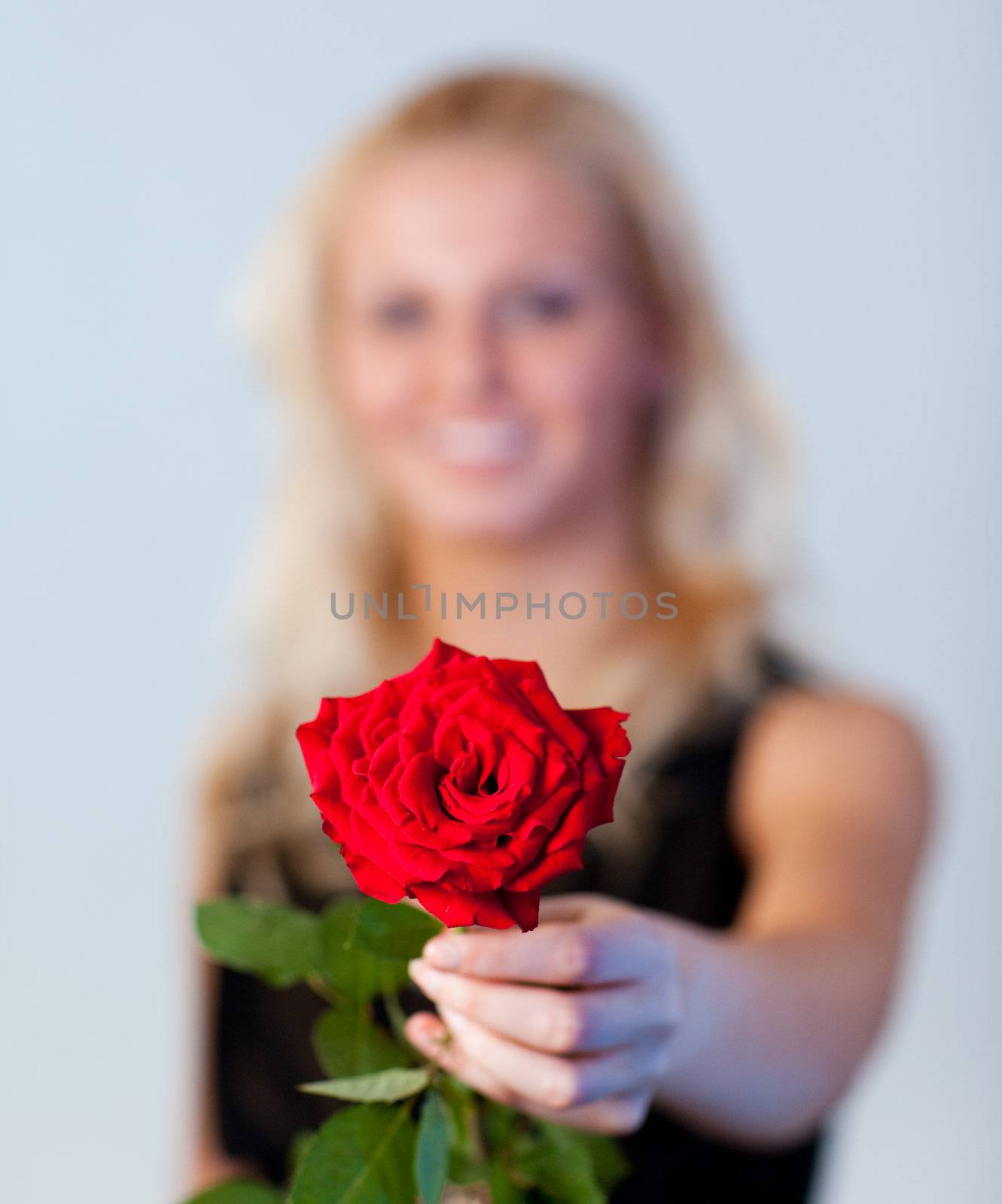 Young blonde woman holding a red rose with focus on rose