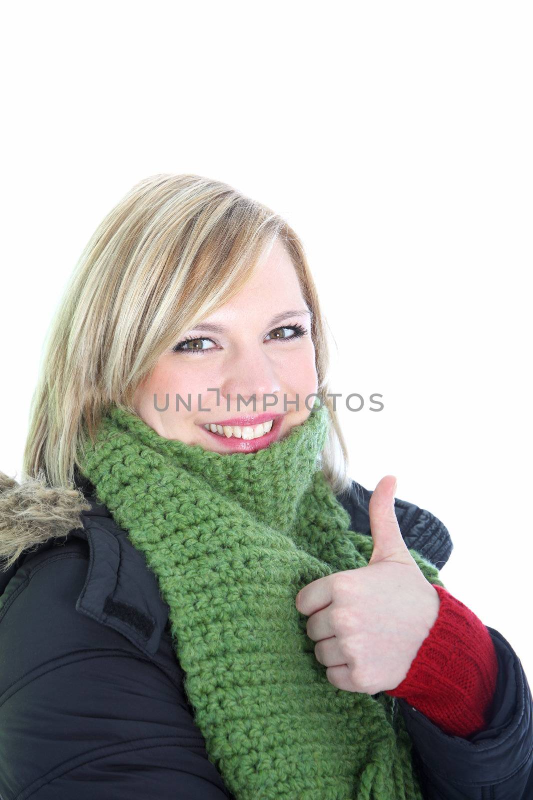 Smiling attractive young woman in winter attire wrapped up in a thick coat and scarf giving a thumbs up gesture of approval