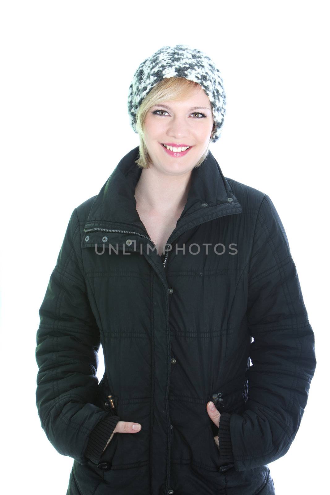 Pretty smiling woman in winter coat and knitted cap standing in a relaxed position with her hands in her pockets isolated on white