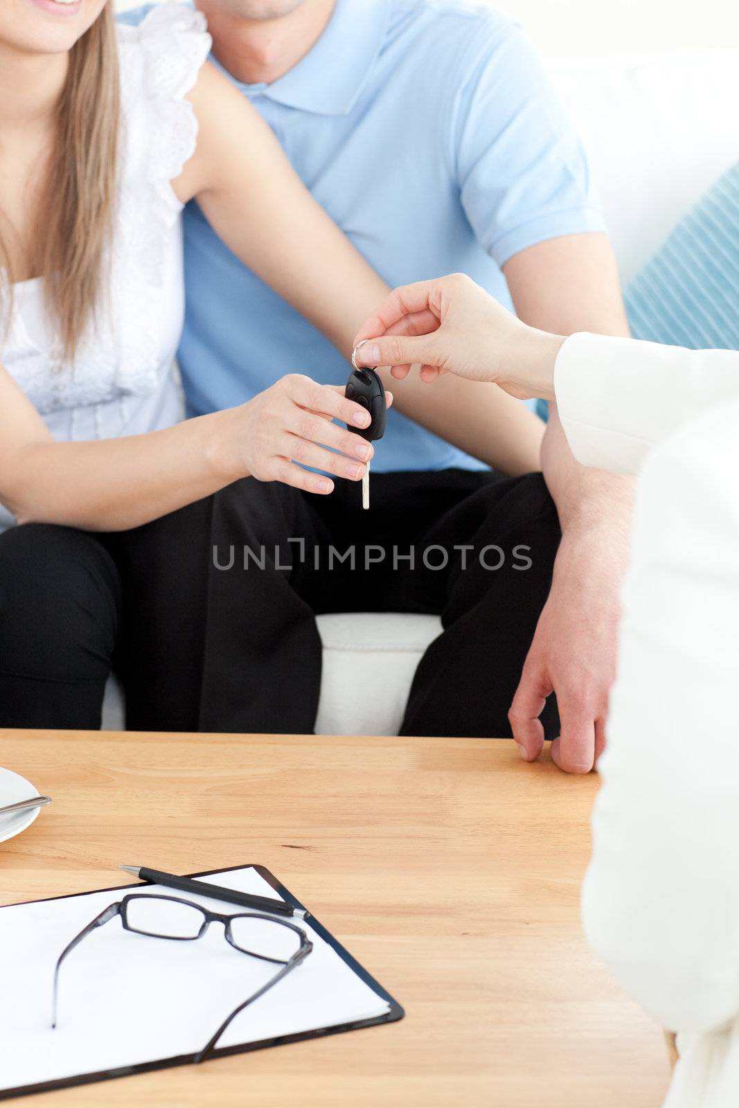 Close-up of a couple receiving their new car's key sitting on a sofa