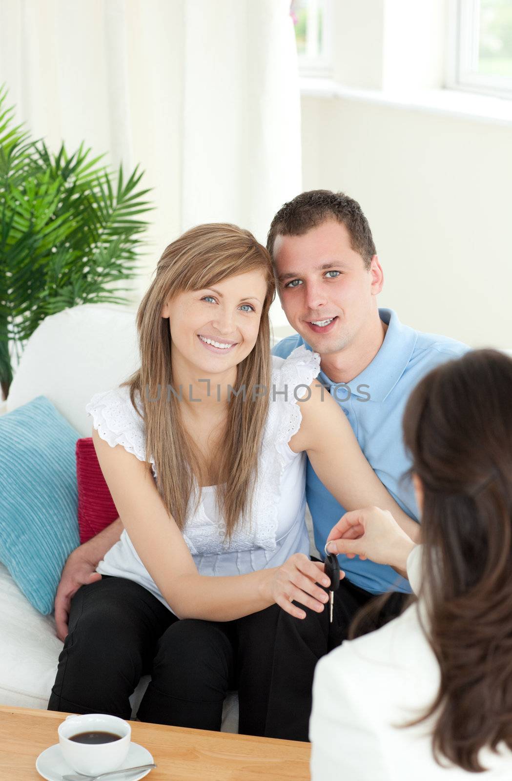 Jolly young couple receiving their new car's key sitting on a sofa