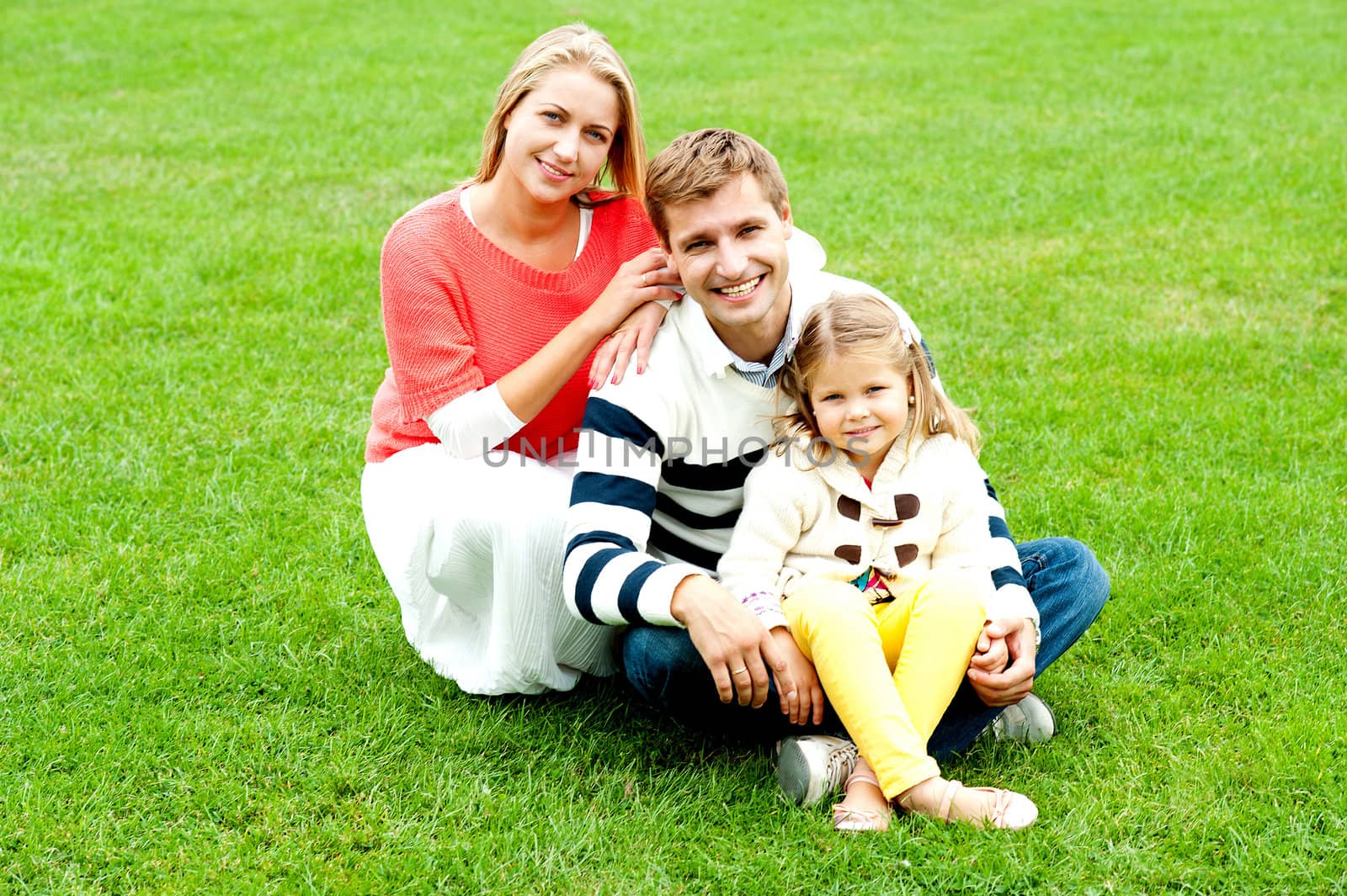 Portrait of happy young family with daughter relaxing on lush green lawn