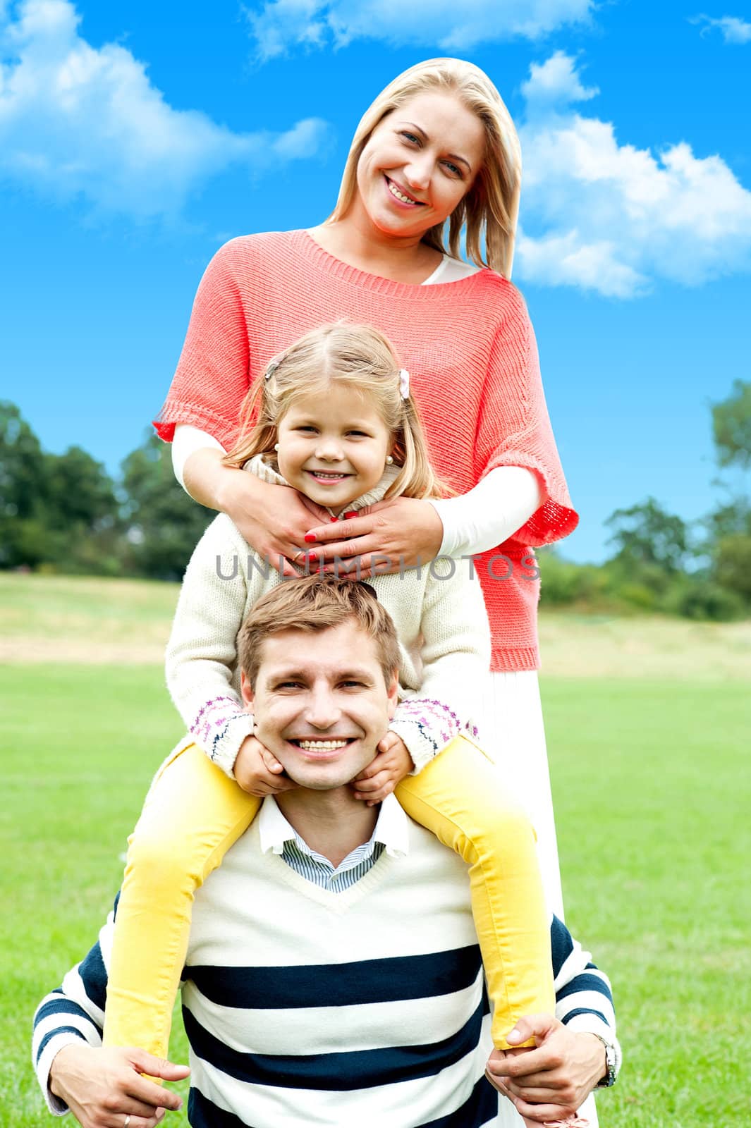 An attractive happy smiling family of mother, father and daughter having fun outside in a park