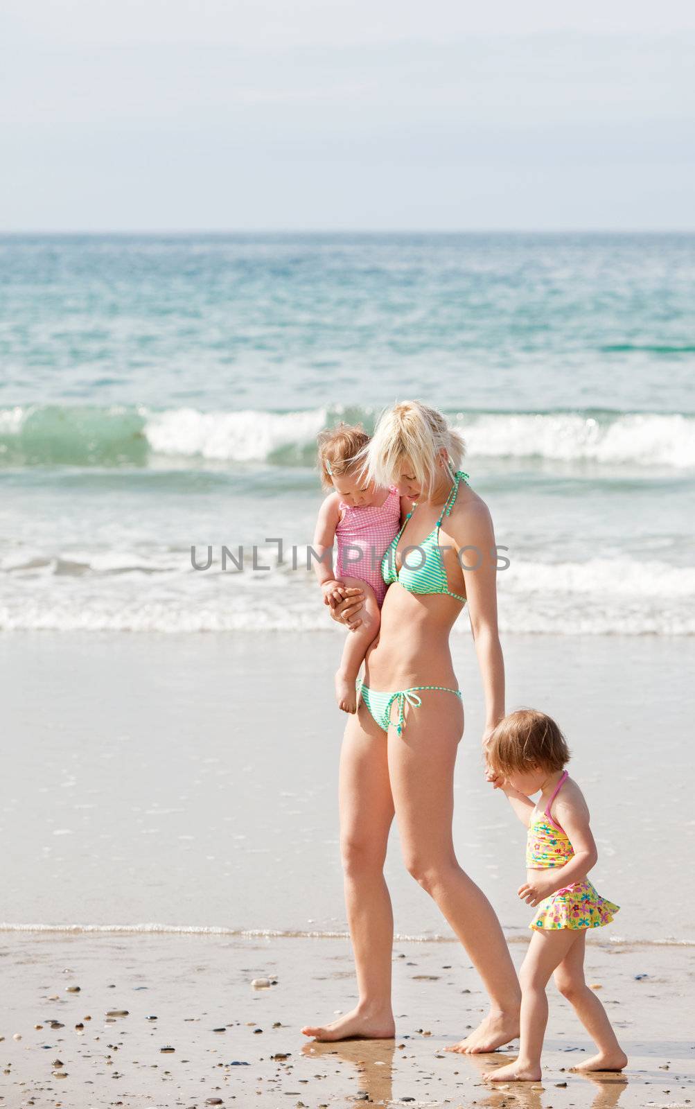 A young mother walking at the beach with her two children on her arm and at her hand