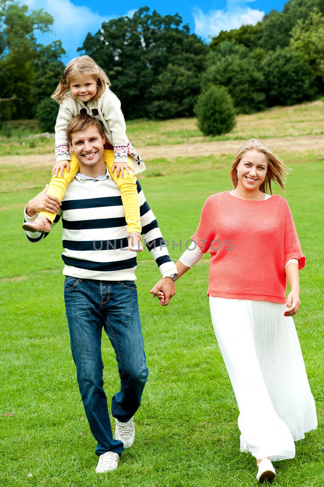 Portrait of family of three. Husband and wife holding hands while walking while daughter enjoys piggy ride