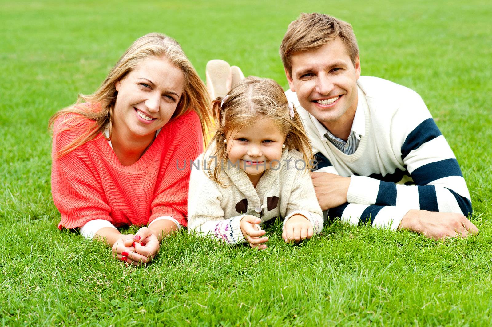 Portrait of a happy family of three lying in the lawn, having fun