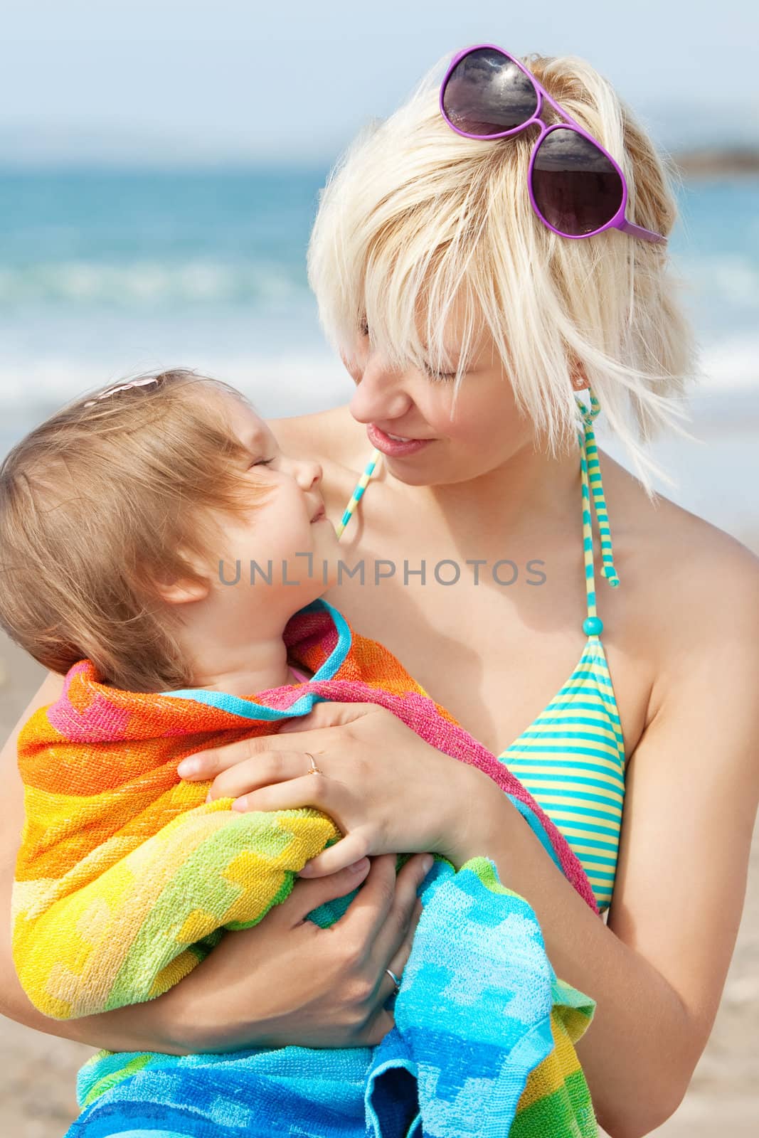 A portrait of a smiling girl in a towel in the arms of her mother at the beach