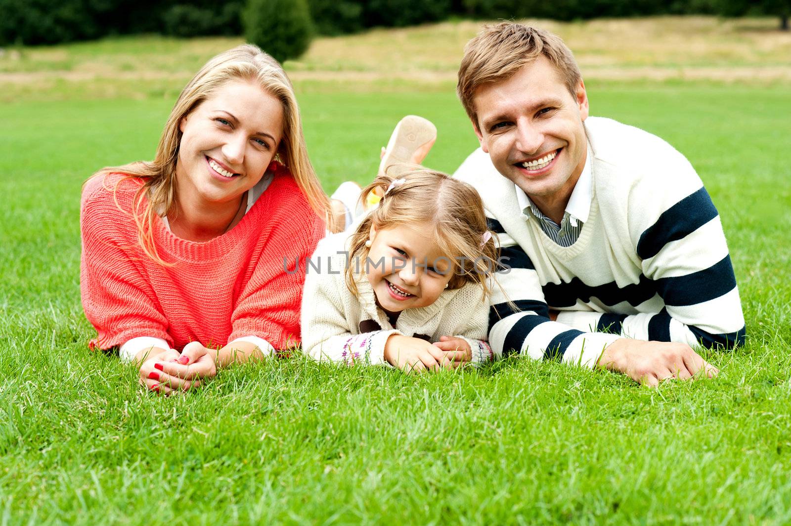 Young family of three spending a happy day outdoors. Relaxing on lush green grass