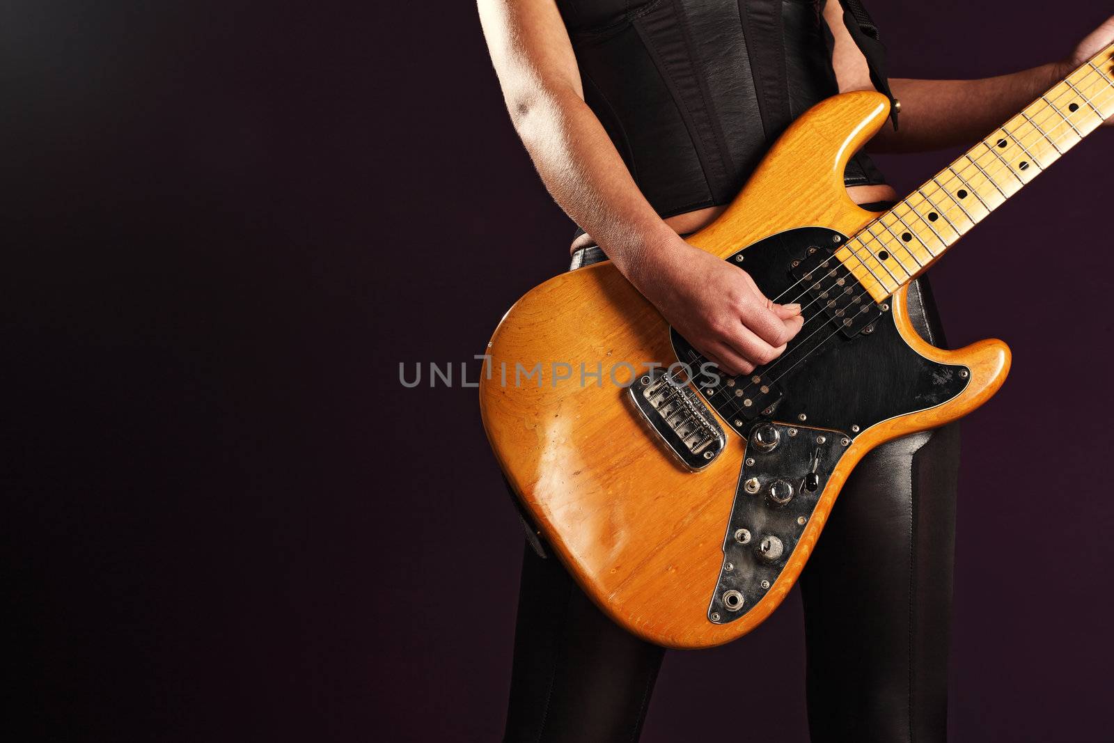 Photo of the body of a female guitar player standing and playing over a dark background.