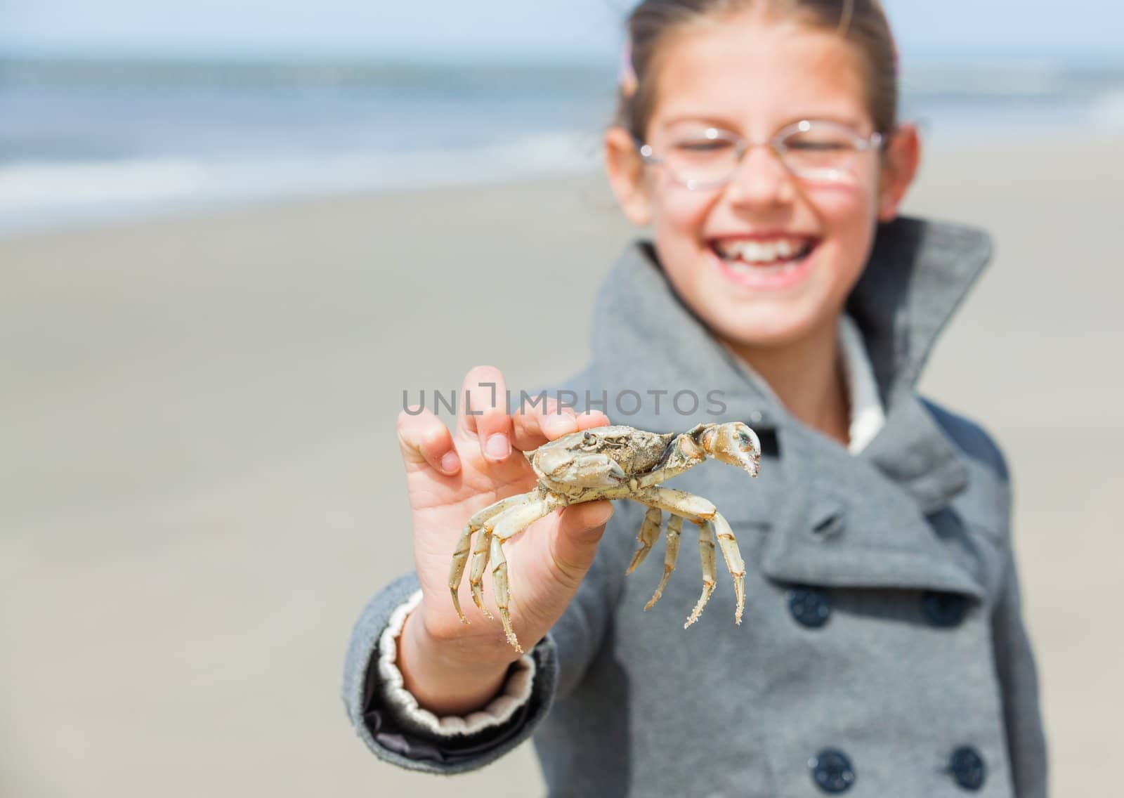 Adorable happy girl holding crab on the beach on spring day. Focus on the crab.