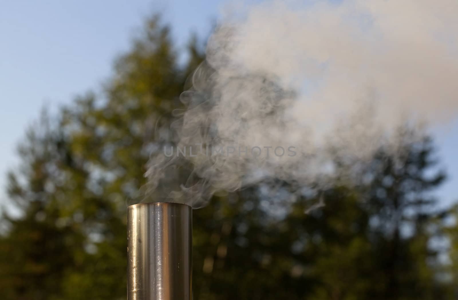 Smoke from a pipe on the background of green forest and blue sky