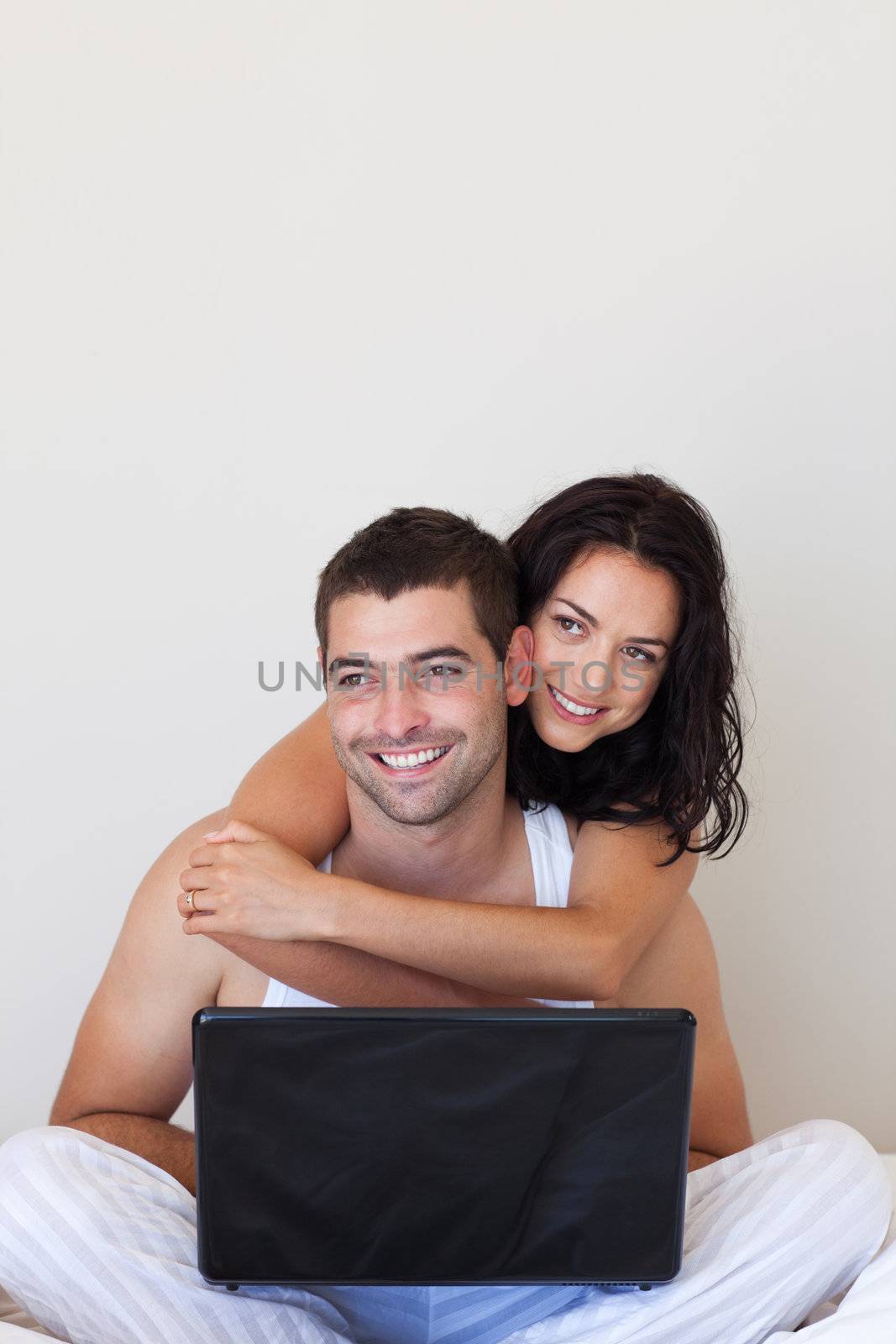 Romantic lovers embracing lying in bed with a laptop