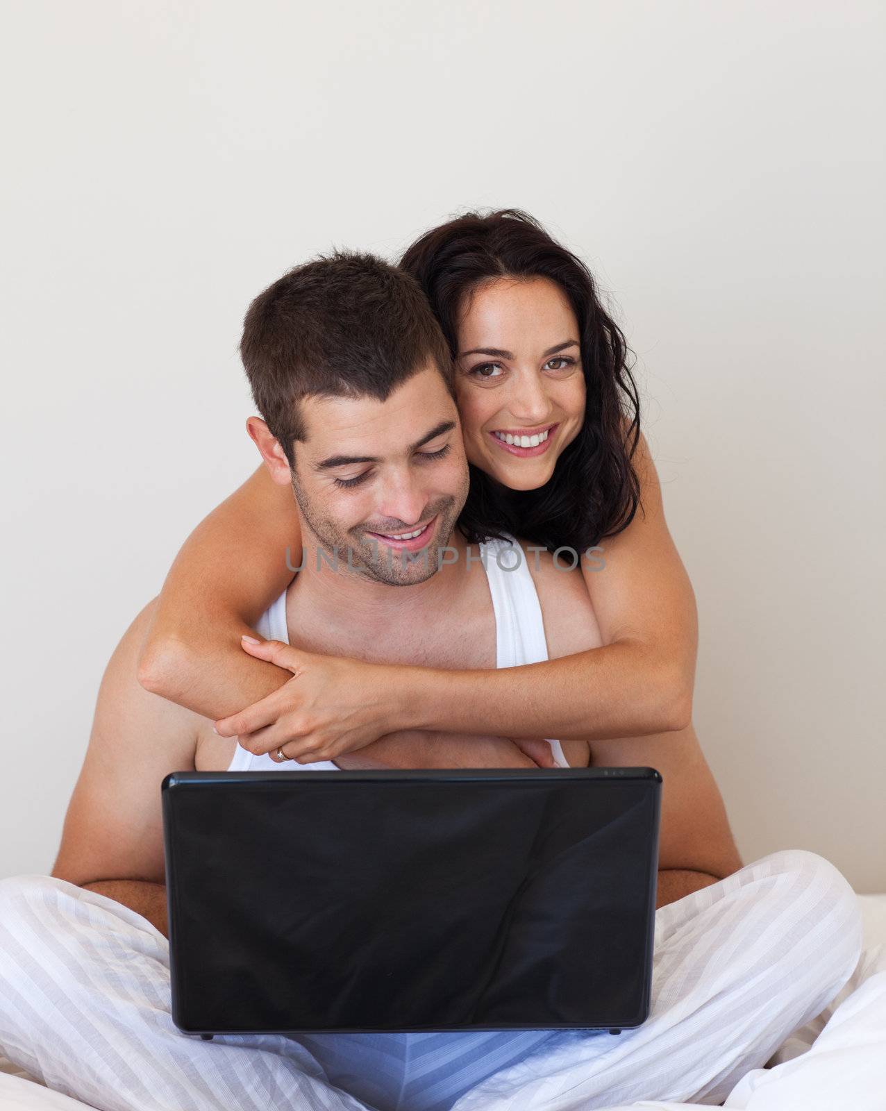 Romantic couple using a laptop lying on their bed 