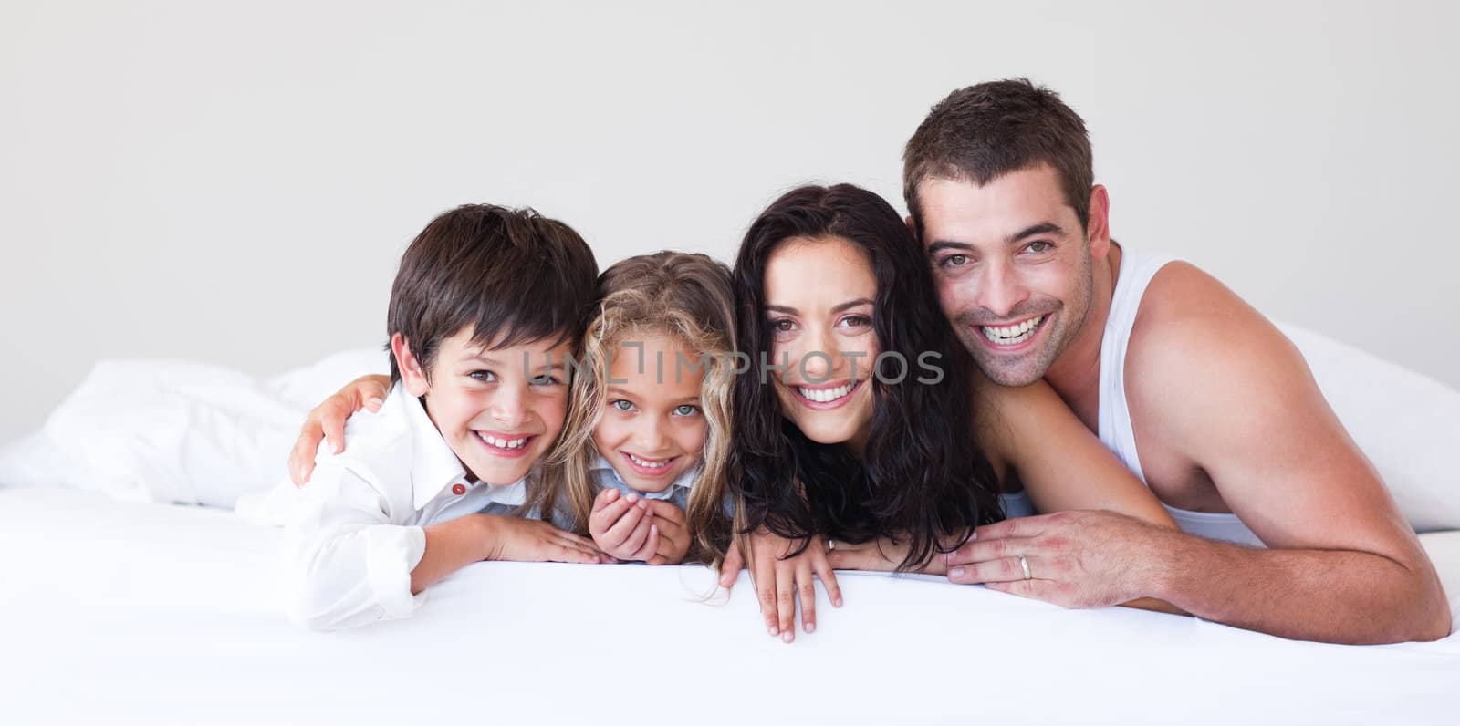 Affectionate parents and their children lying on a bed smiling at the camera 