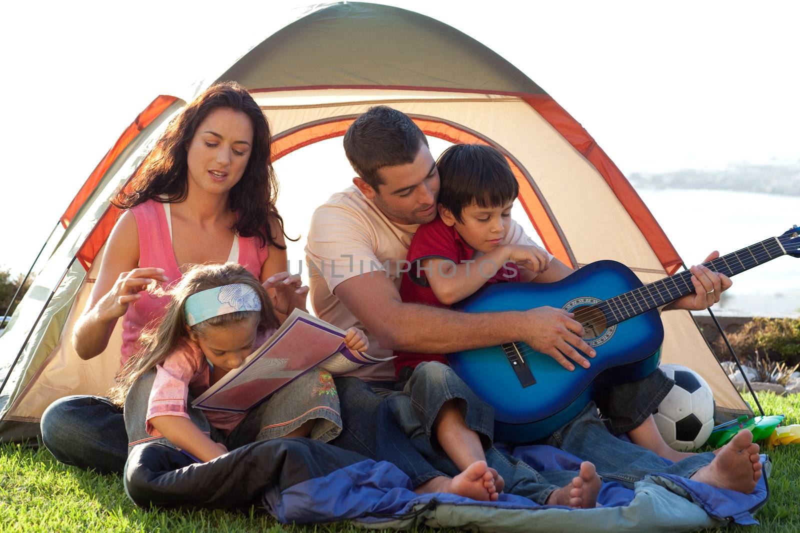 Young family in a tent playing with a guitar and drawing
