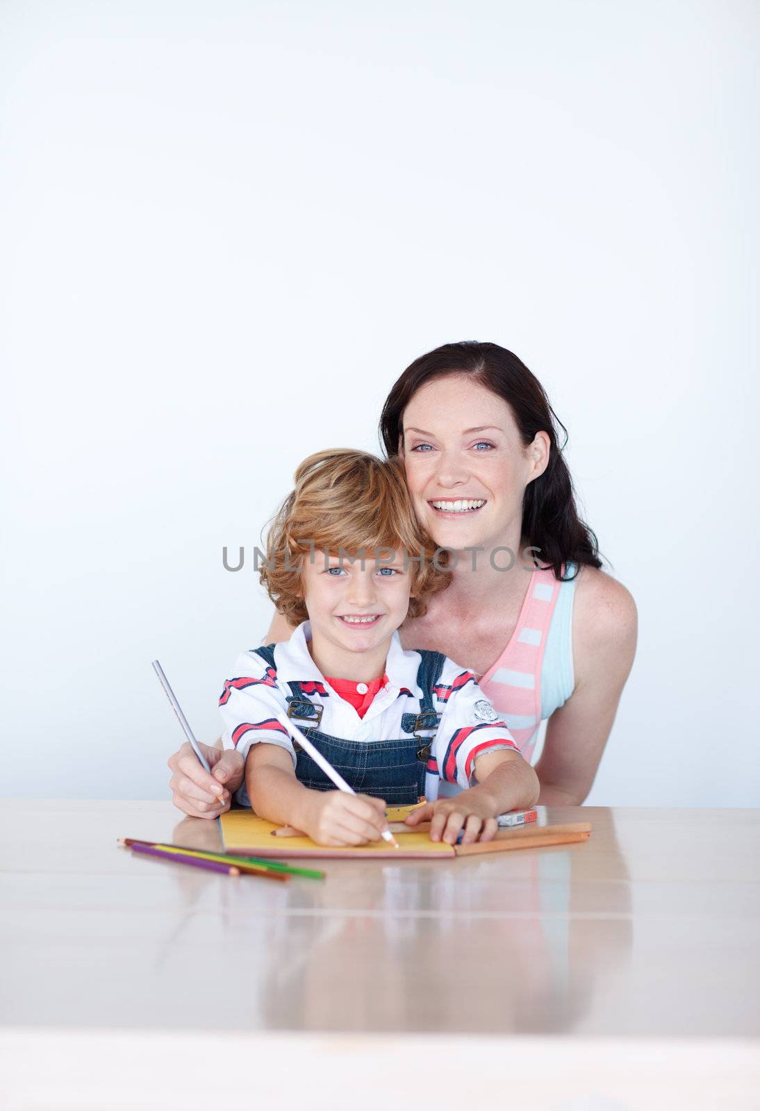 Bright other and son writing at home and smiling to the camera 