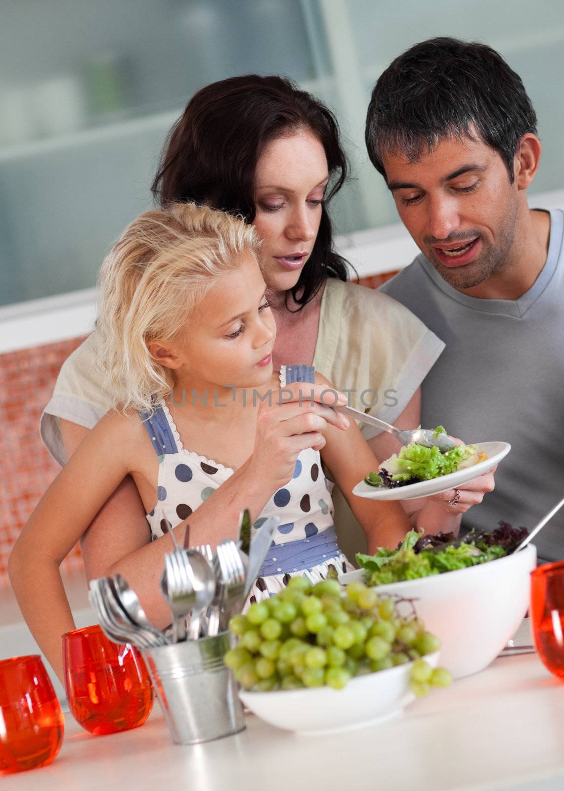 Cute girl with her parents in the kitchen eating 