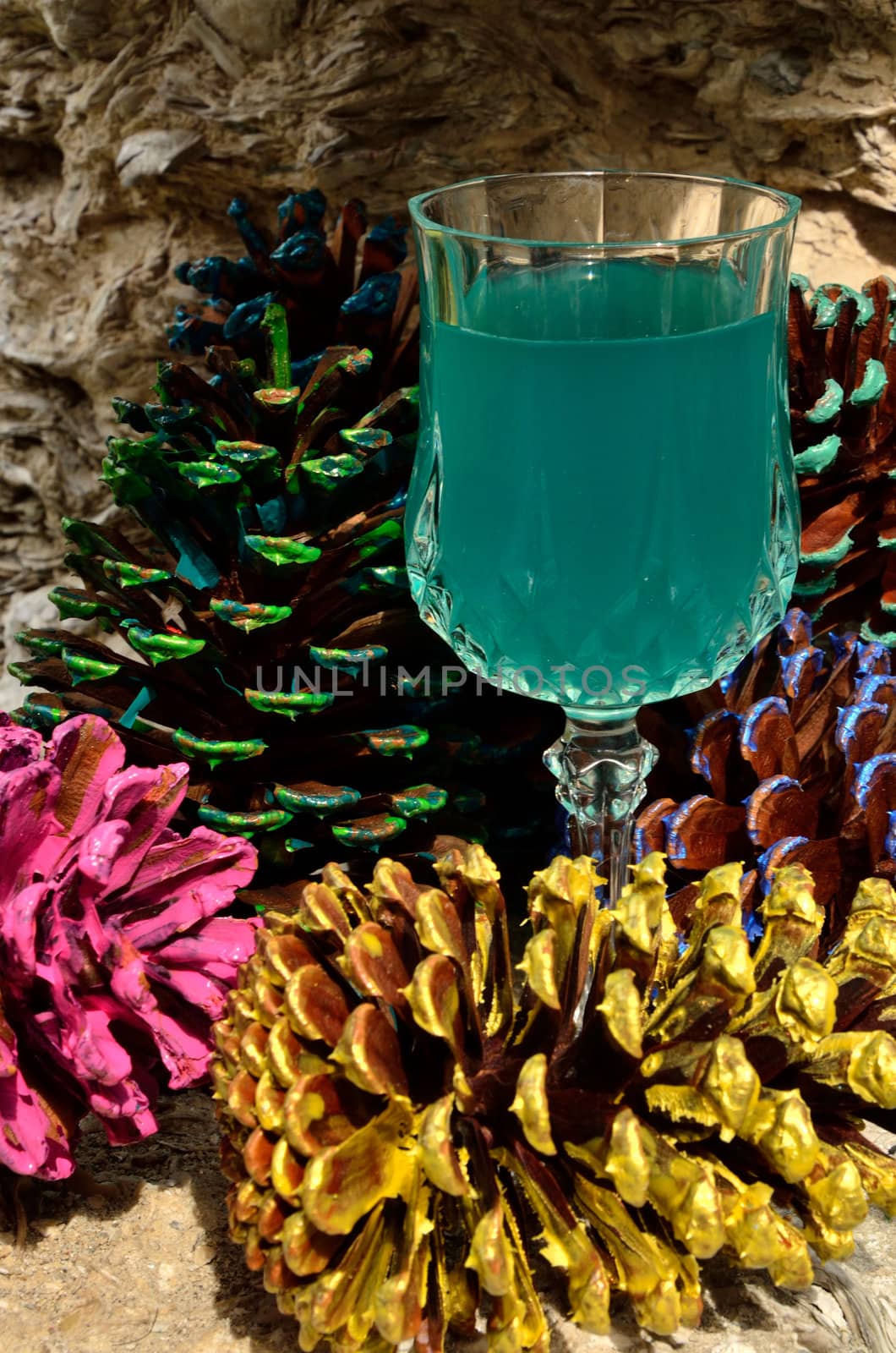 A blue beverage in a crystal goblet amongst decorative pine cones