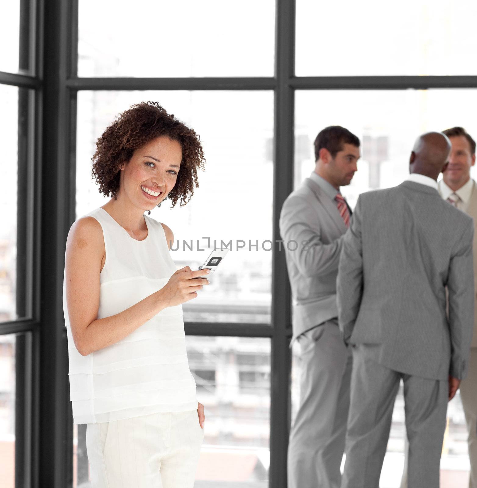 Cheerful Businesswoman holding a phone at workplace with his colleagues in the background