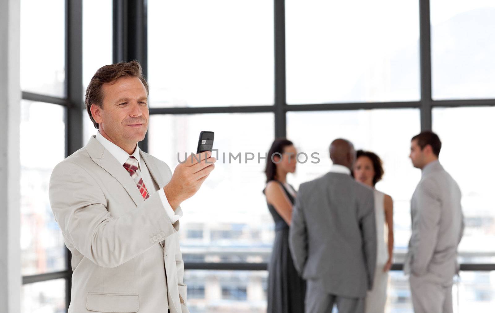 Caucasian businessman holding a phone at workplace with his colleagues in the background