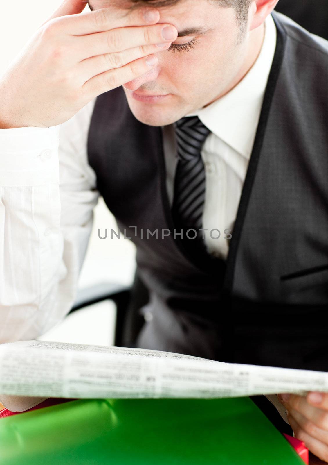 Thinking businessman reading a newspaper sitting at his desk
