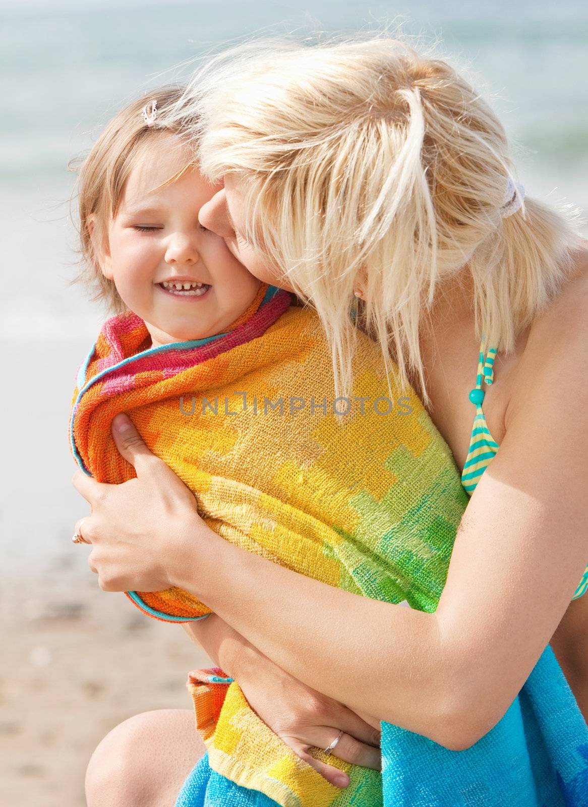 A portrait of a  mother kissing her laughing daughter at the beach