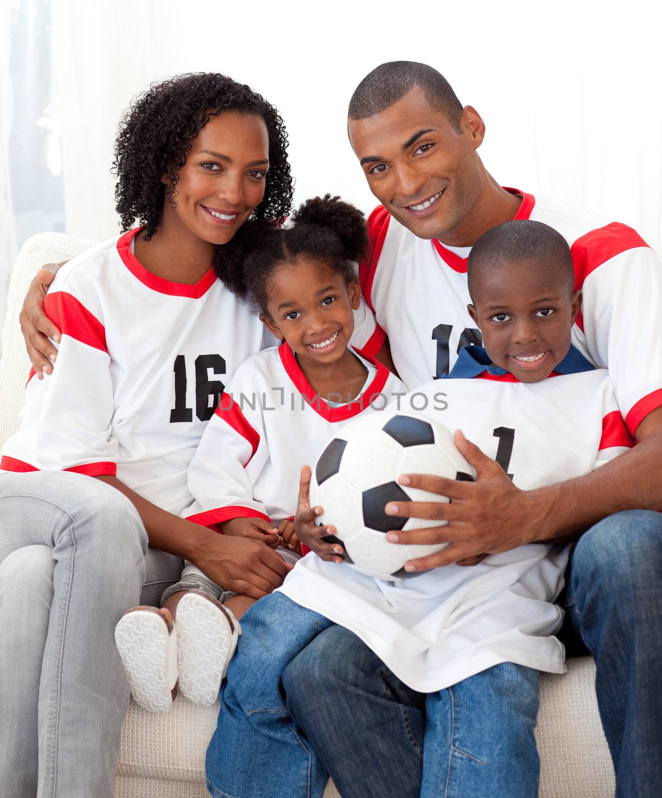 Smiling Afro-american family holding a soccer ball on sofa