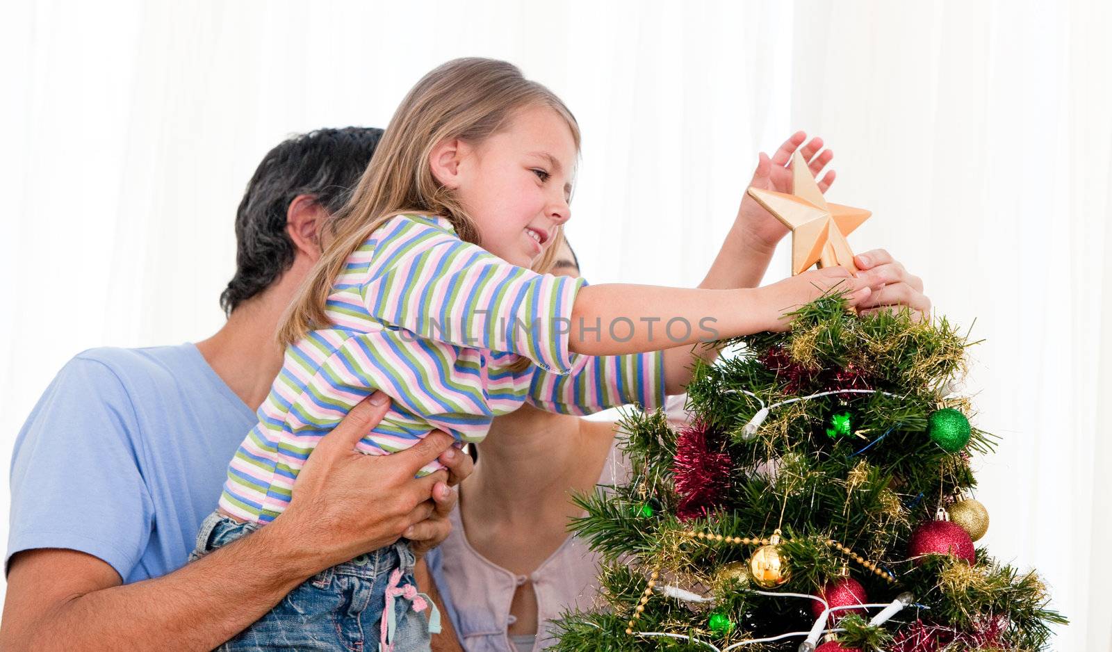 Little girl placing a star in a Christmas tree with her parents