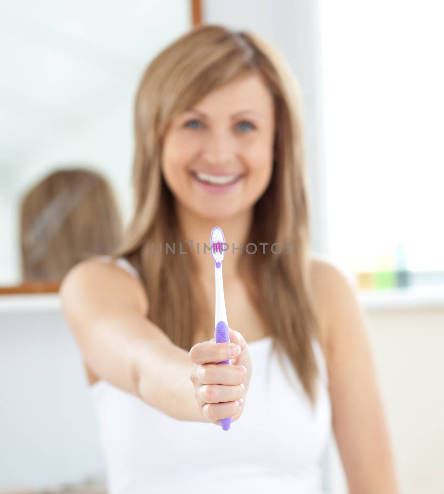 Smiling woman holding a toothbrush into the camera  by Wavebreakmedia