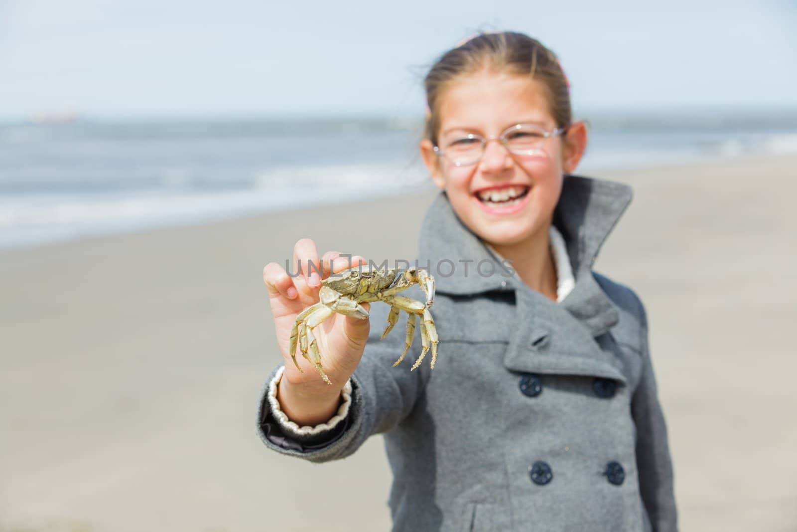 Adorable happy girl holding crab on the beach on spring day. Focus on the crab.