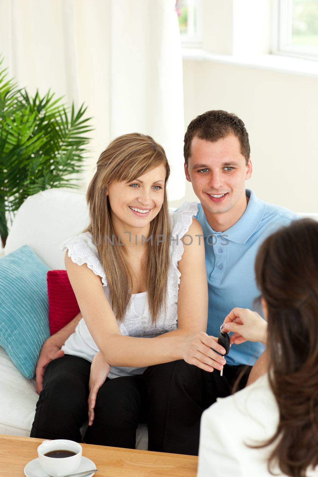 Loving young couple receiving their new car's key sitting on a sofa 