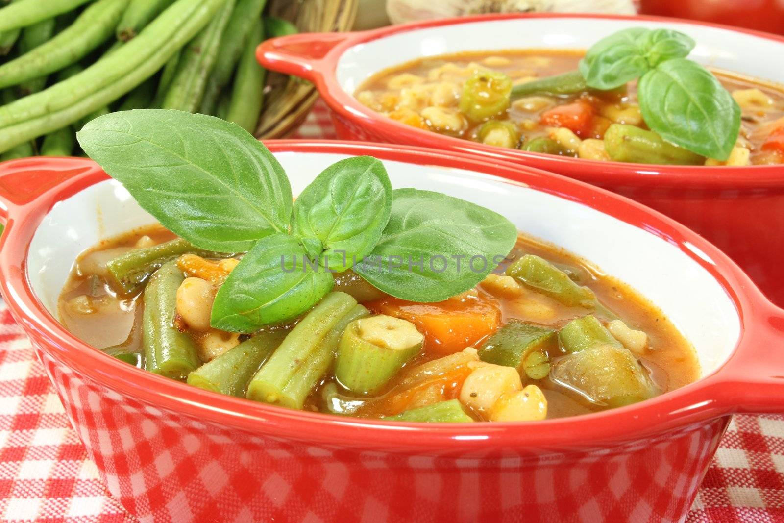 Minestrone with green beans, carrots, potatoes, and fresh basil on a bright background