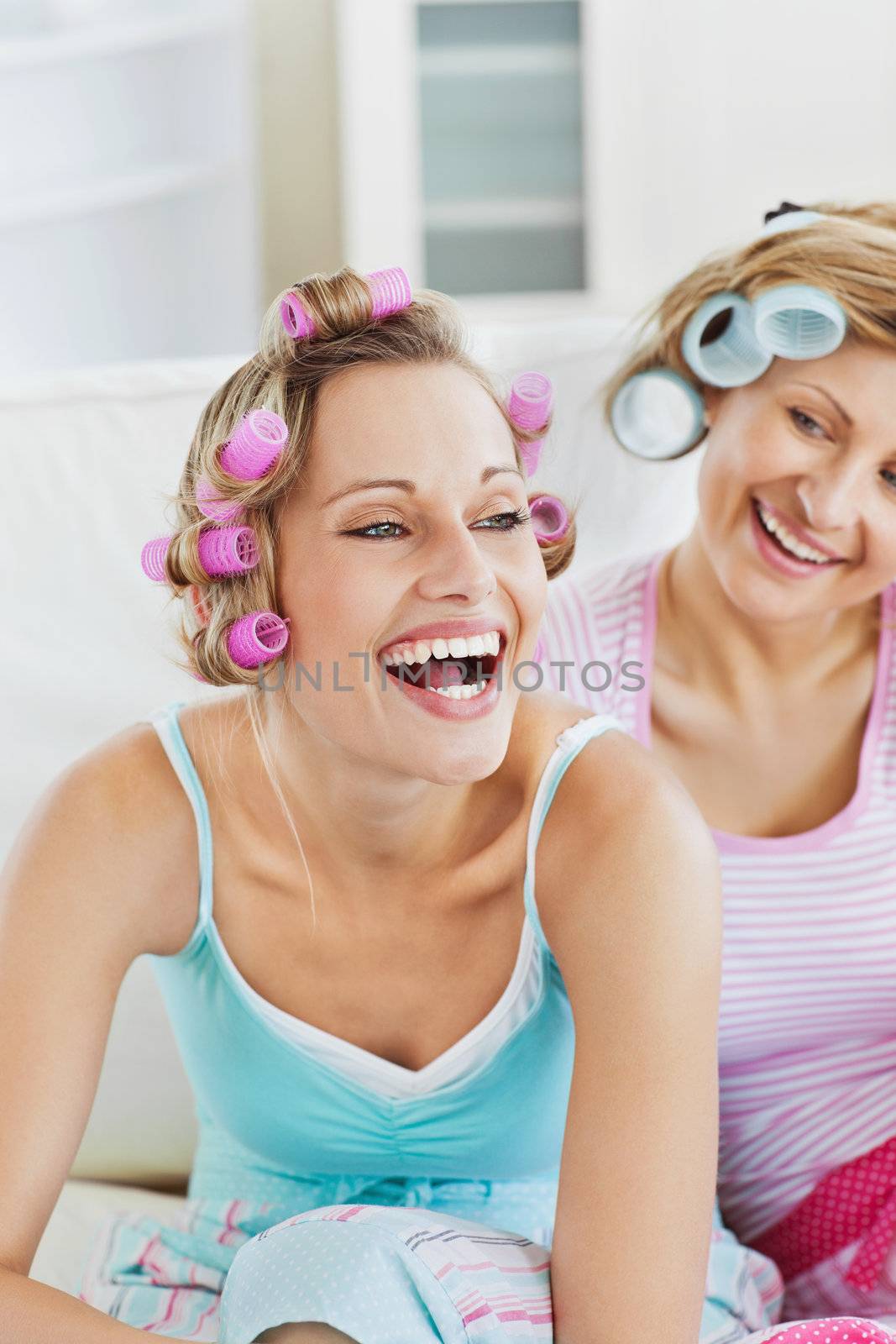 Laughing women wearing hair rollers sitting on the sofa at home