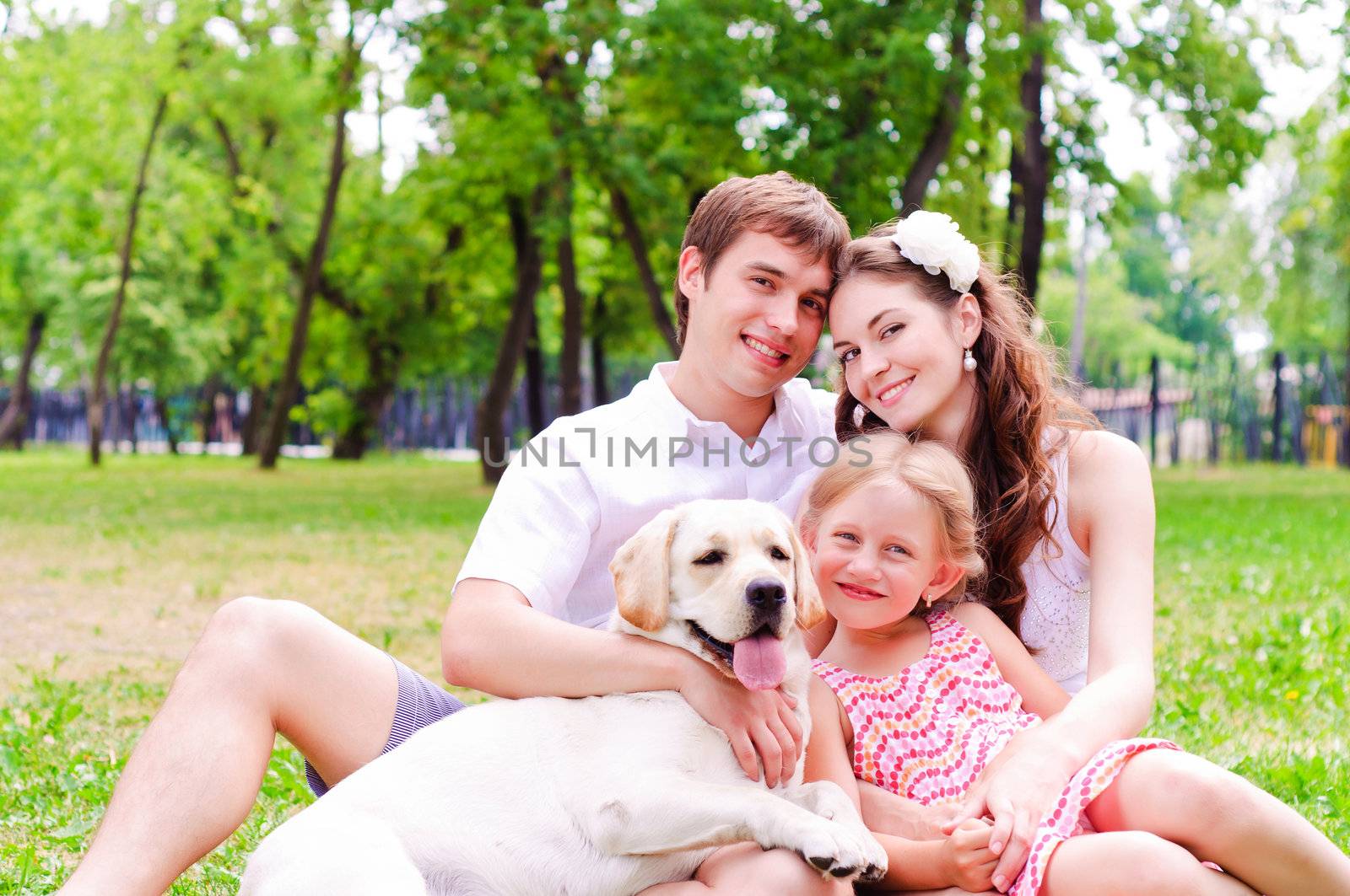Happy young family with Labrador is resting in the park