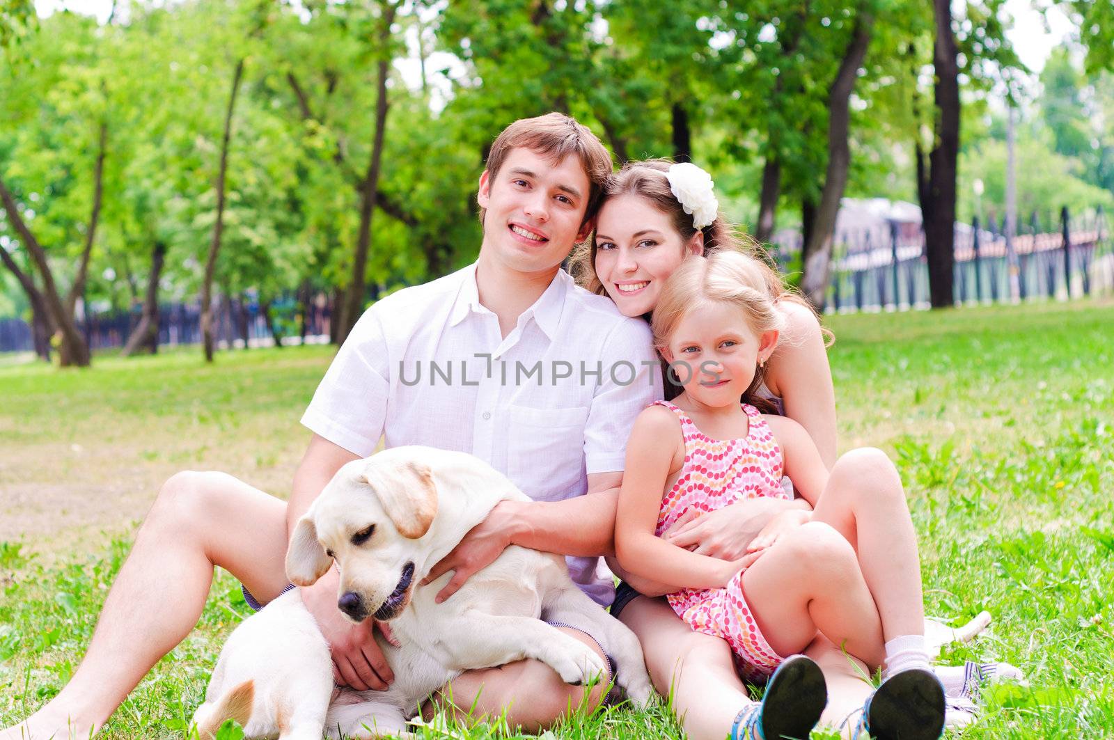 Happy young family with Labrador is resting in the park