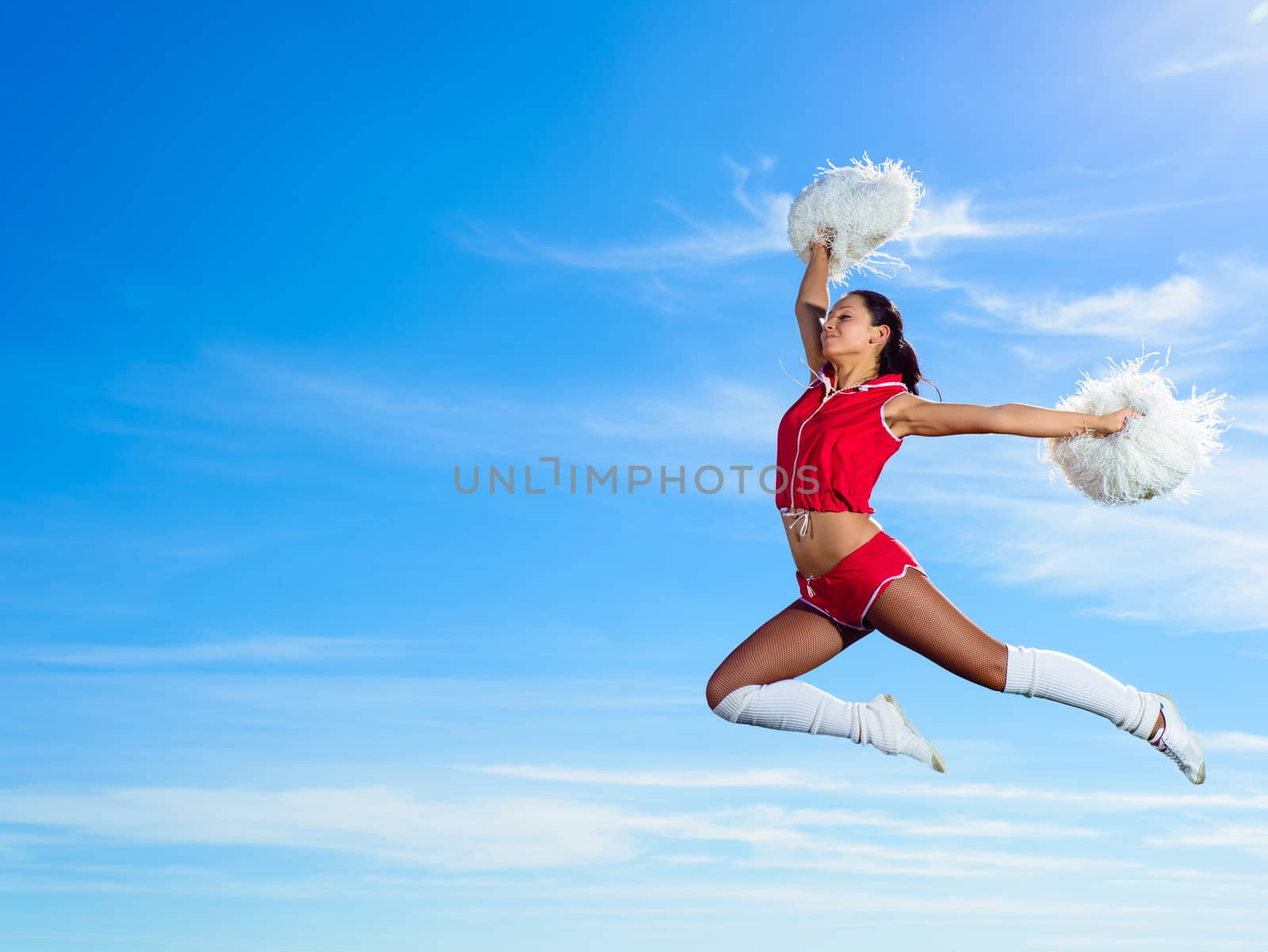 Young cheerleader in red costume jumping against blue sky