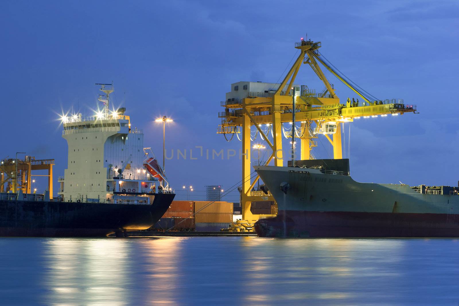 Industrial Container Cargo freight ship with working crane bridge in shipyard at dusk for Logistic Import Export background