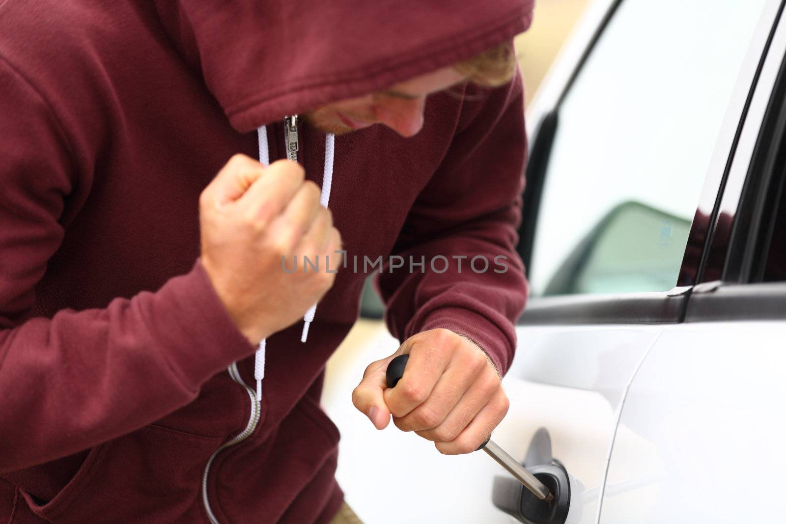 Young thug stealing a car forcing a screw driver into the door lock and hammering at it with his fist