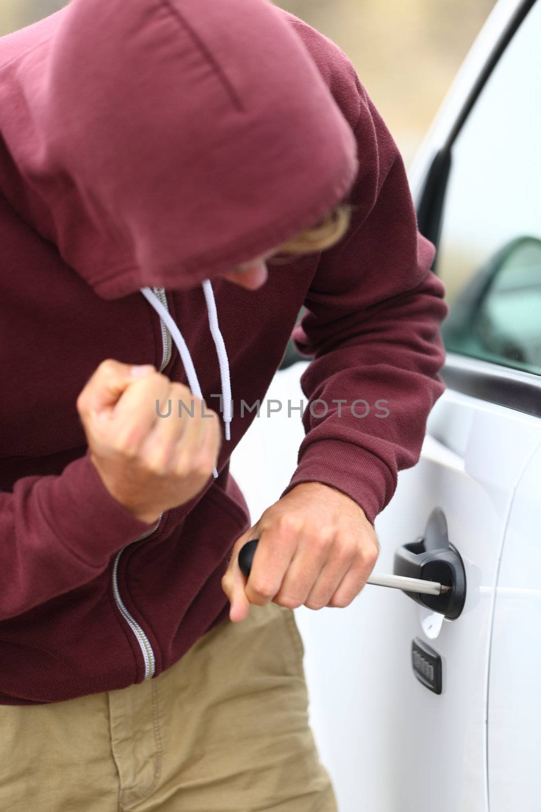 Youth wearing a hoodie breaking into a car by destroying the door lock with a screw driver