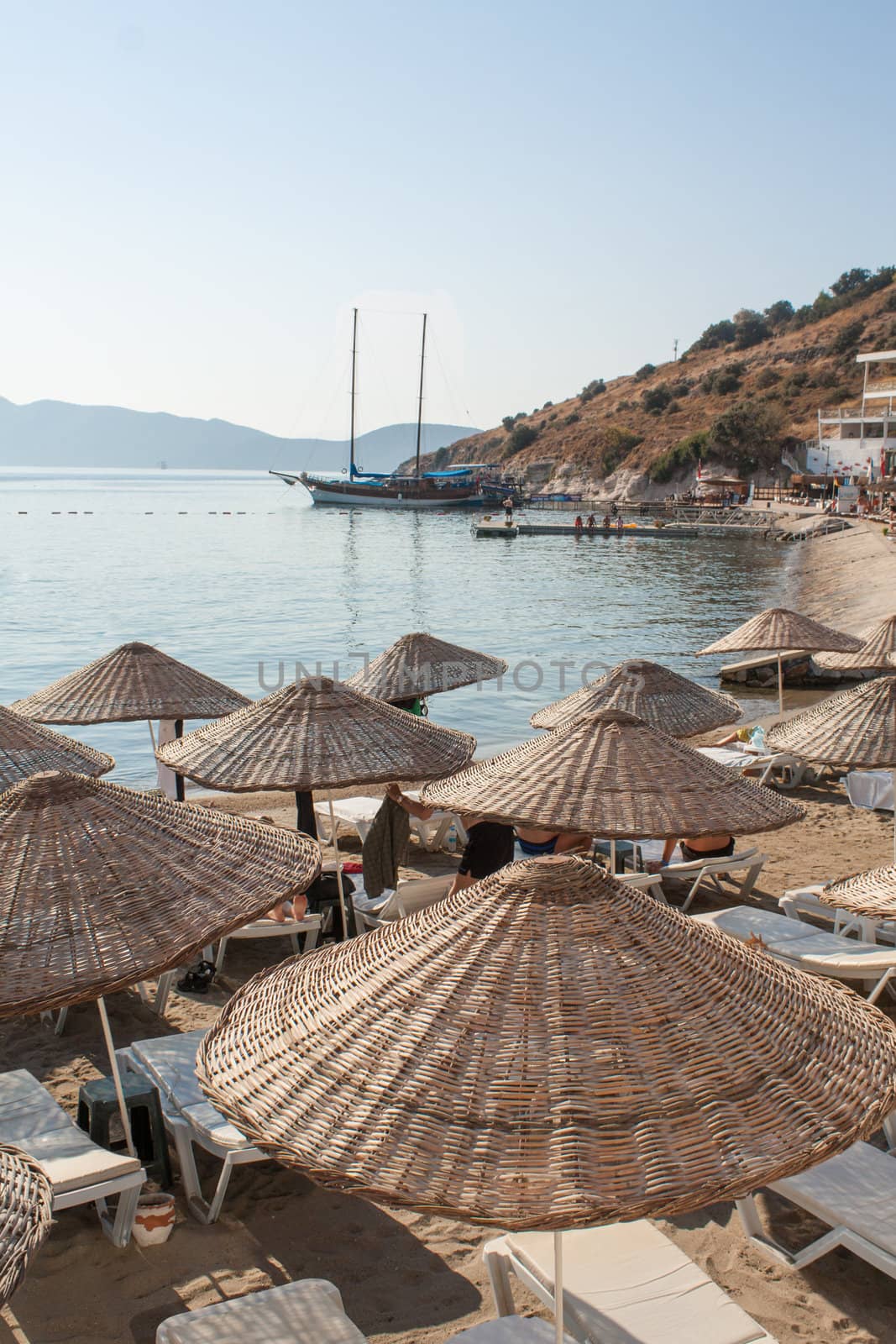 Bardakci Bay Beach in Bodrum, Turkey, with wicker parasols and white loungers.