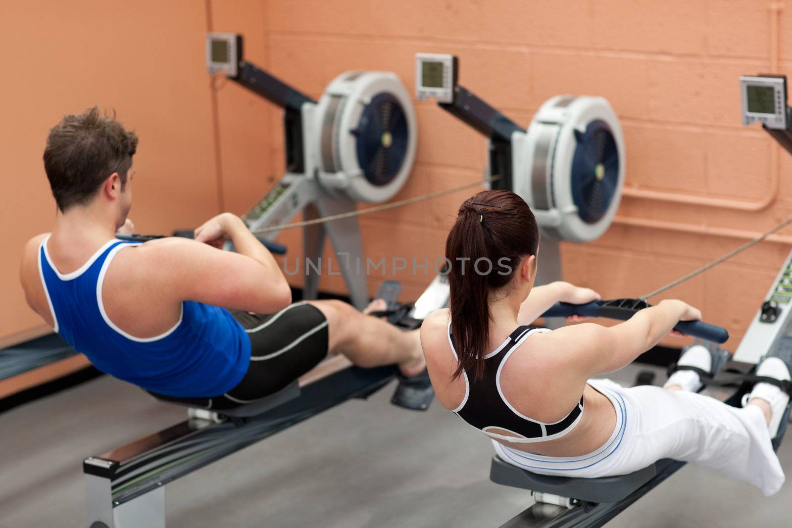 Concentrated people using a rower in a fitness center