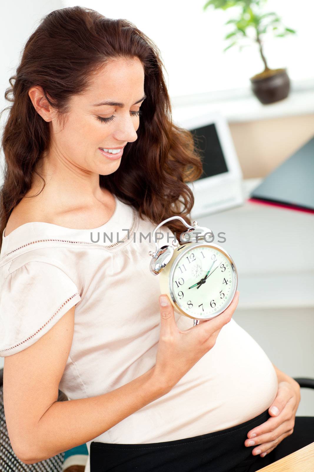 Pregnant businesswoman holding an alarm clock and looking at her by Wavebreakmedia